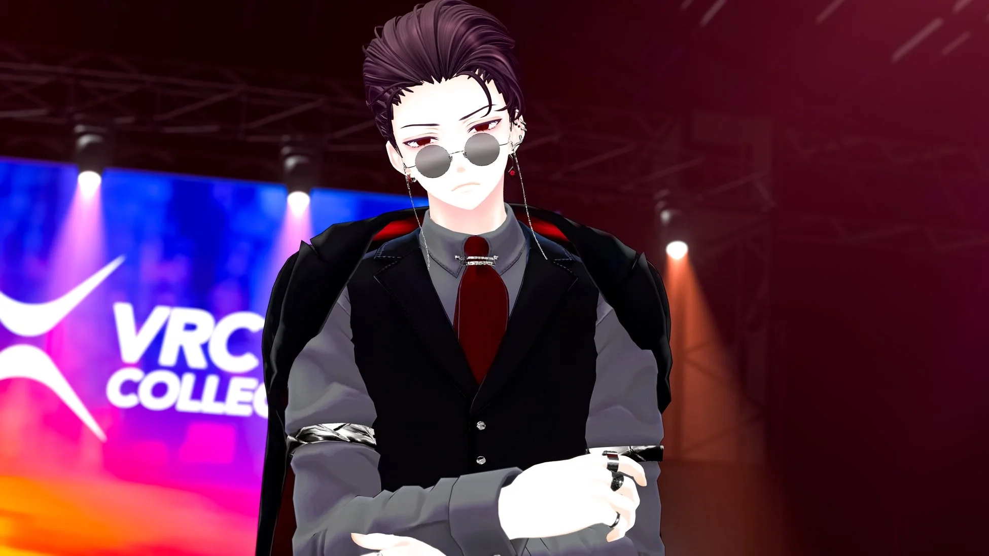 ステージ上でクールなポーズをとるアニメ調の男性キャラクター。サングラスとスーツを着用し、背景には「VRC COLLEGE」のロゴが見える。