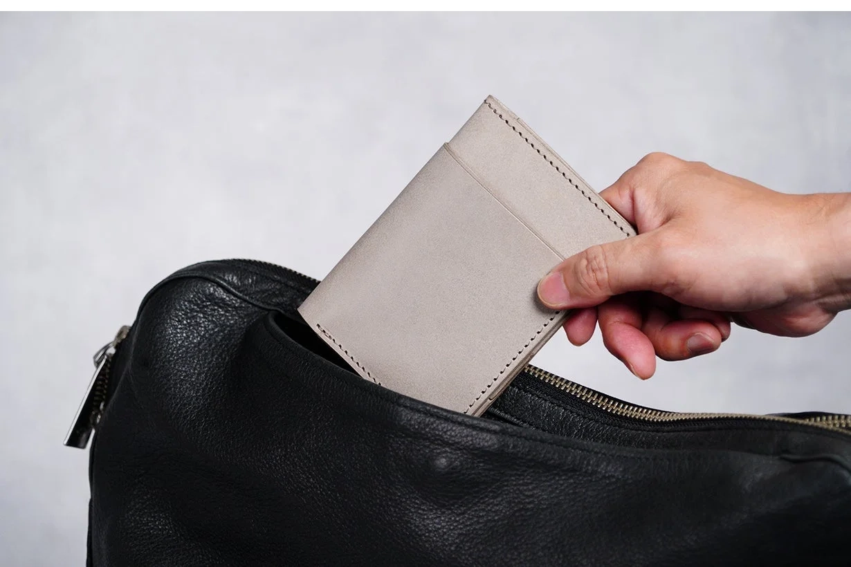 手がグレーの小物入れのようなものを黒い革製バッグに入れている様子